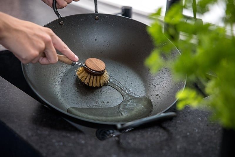 Hand rengör en stor stekpanna med vatten och diskborste